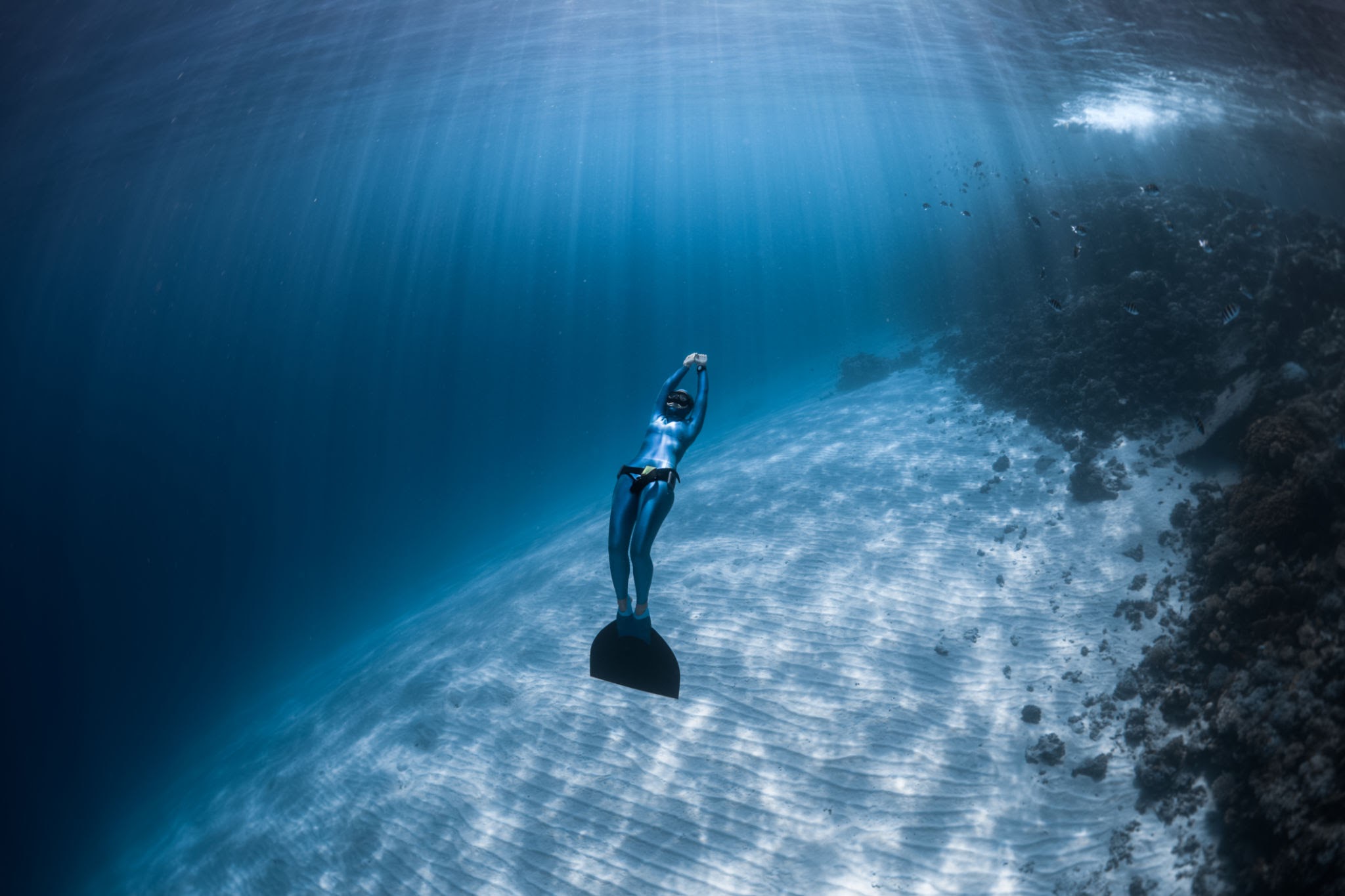 Woman freediver glides over sandy bottom of a crystal clear tropical sea