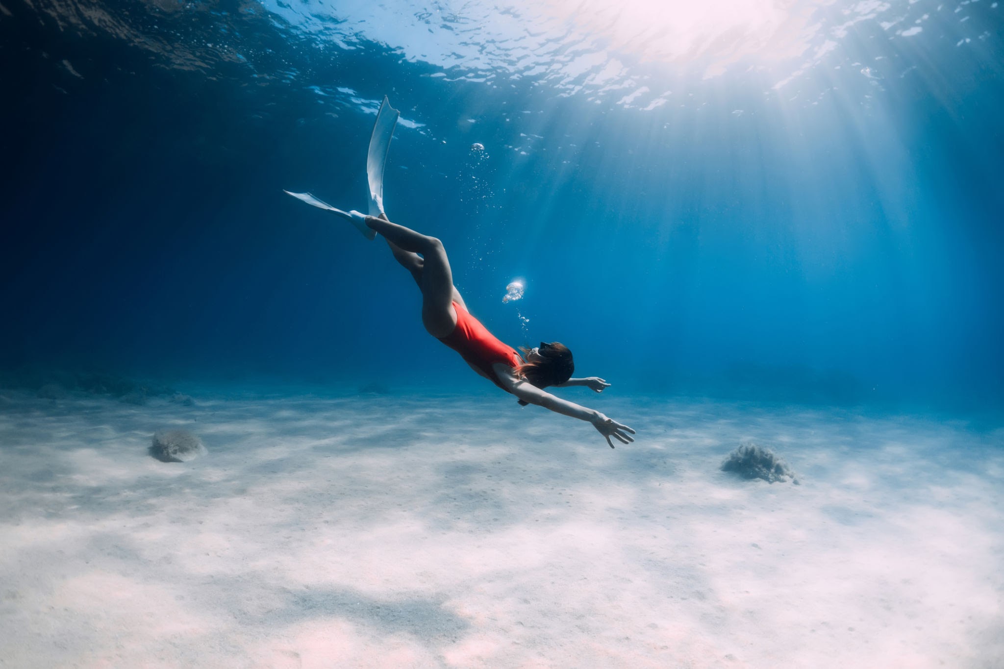 Woman with fins and air bubble underwater in blue ocean.